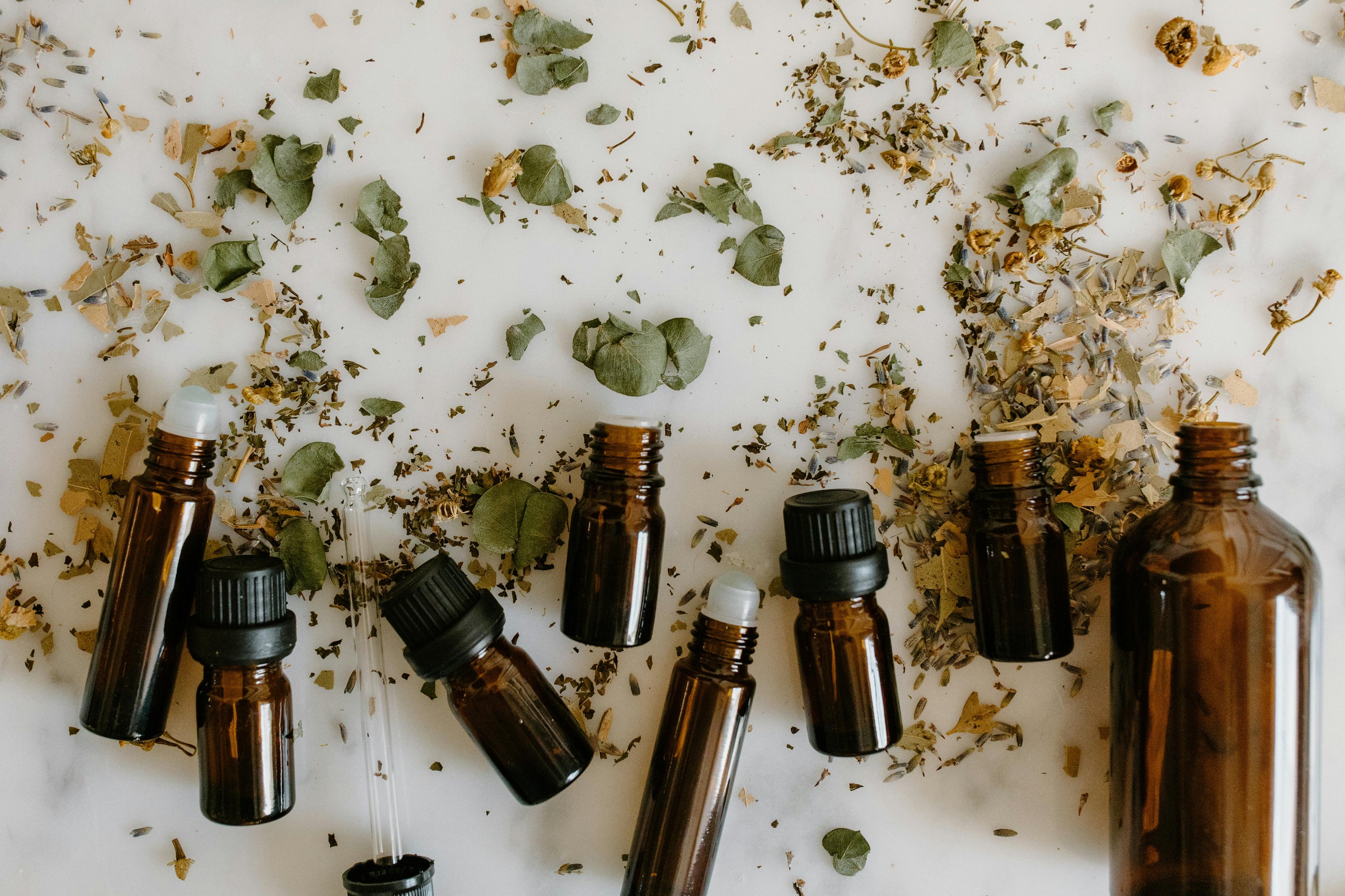 Flacons ambrés d’extraits de plantes entourés d’herbes séchées, évoquant les préparations naturelles pour la santé féminine à chaque âge.