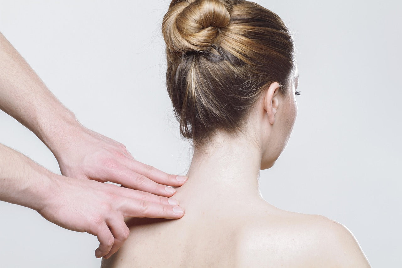 Mains d’un praticien massant la nuque d’une femme, évocation du bien-être global et de l’impact des hormones sur la peau et la détente.
